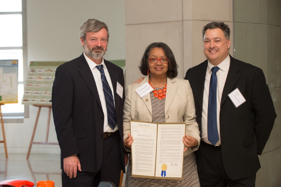 three people pose for a photo. The person in the middle holds up a formal document