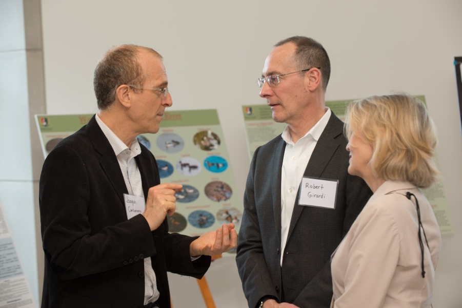 "Joaquin Carbonara" speaks with "Robert Gerardi" and another guest in front of a poster featuring water fowl