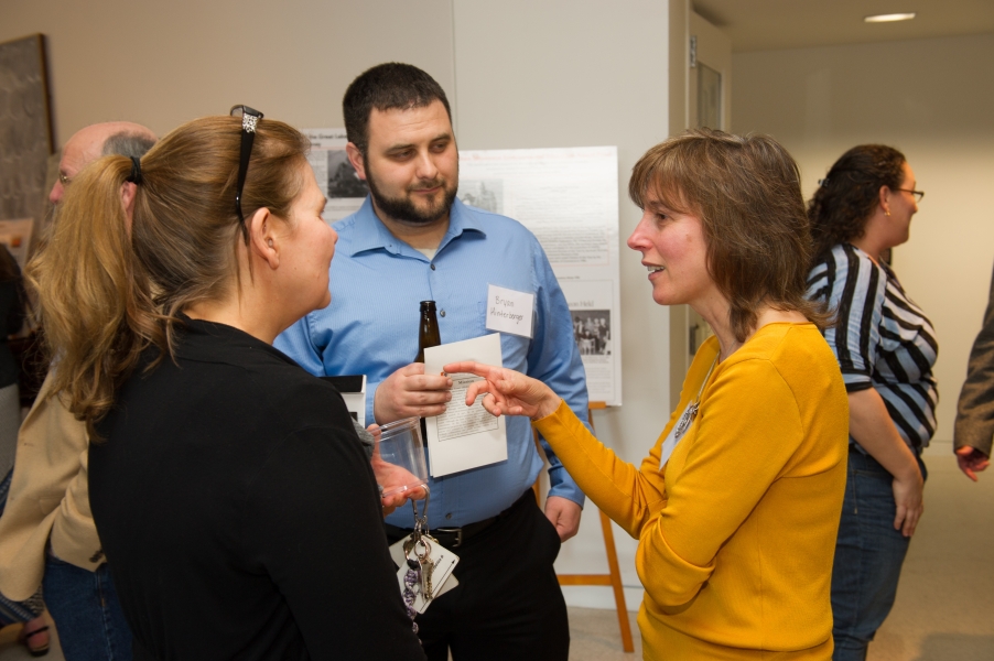 three people talk while other guests mingle in the background. The person in the middle has a name tag that says "Brian Hinterberger"