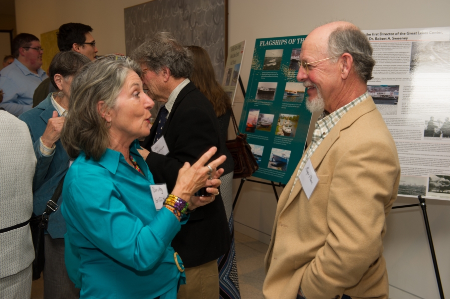 Two people with name tags "Dorothy Griffith" and "Roger Allen" stand talking near posters while other guests mingle in the background