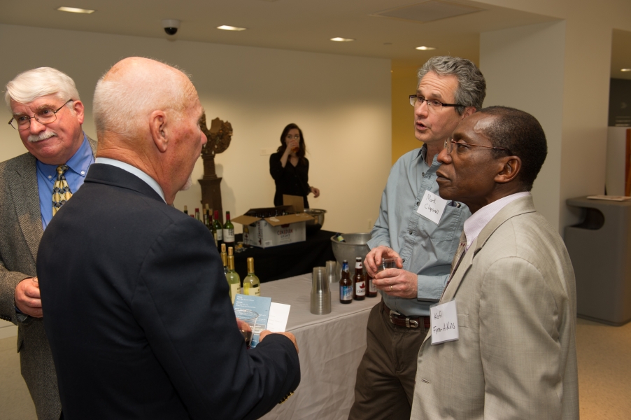 Four people talk near the refreshment table. There are two other people in the background.