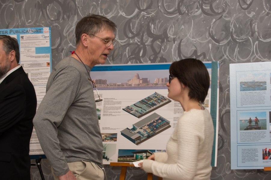 A person talks with a student in front of a poster on an easel