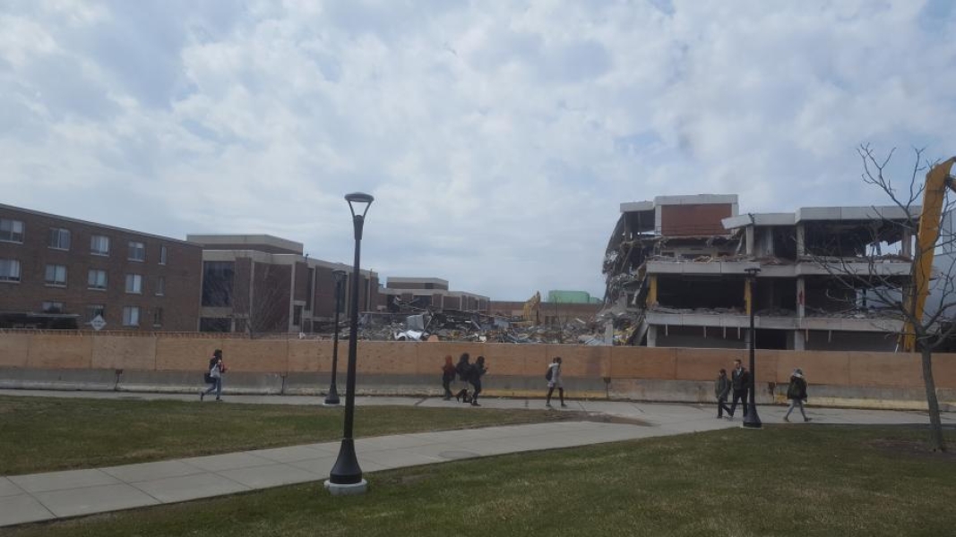 People walking on sidewalks in front of a construction zone with a partially demolished building.