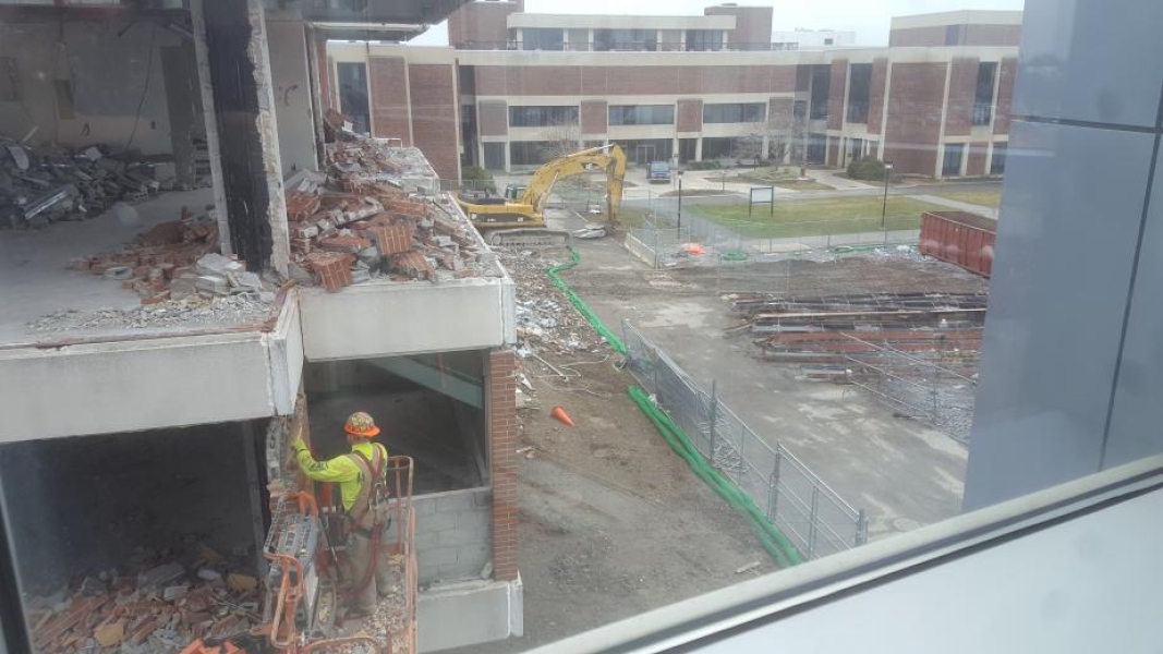 A worker removing bricks from the wall on the second floor of a building. Taken from the third floor window of the building next to it.