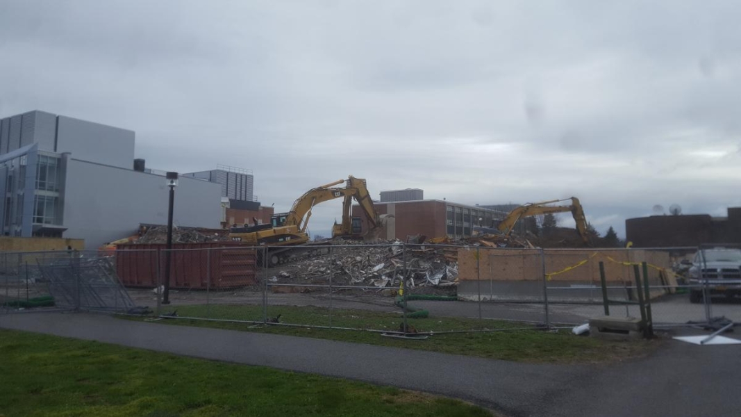 Three excavators work on top of a pile of rubble in a construction zone.