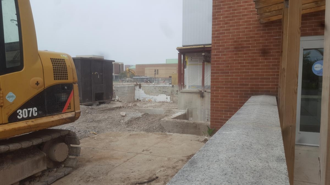 An excavator and a dumpster sit next to an open foundation.