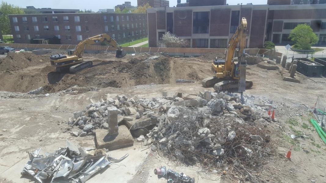 One excavator in a construction site is digging while another excavator breaks concrete into smaller pieces.