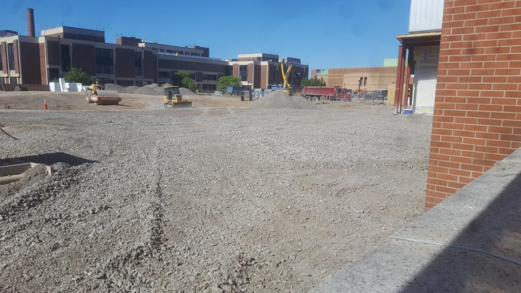 Flat gravel spread next to an existing building. A bulldozer and a steam roller are working in the area.