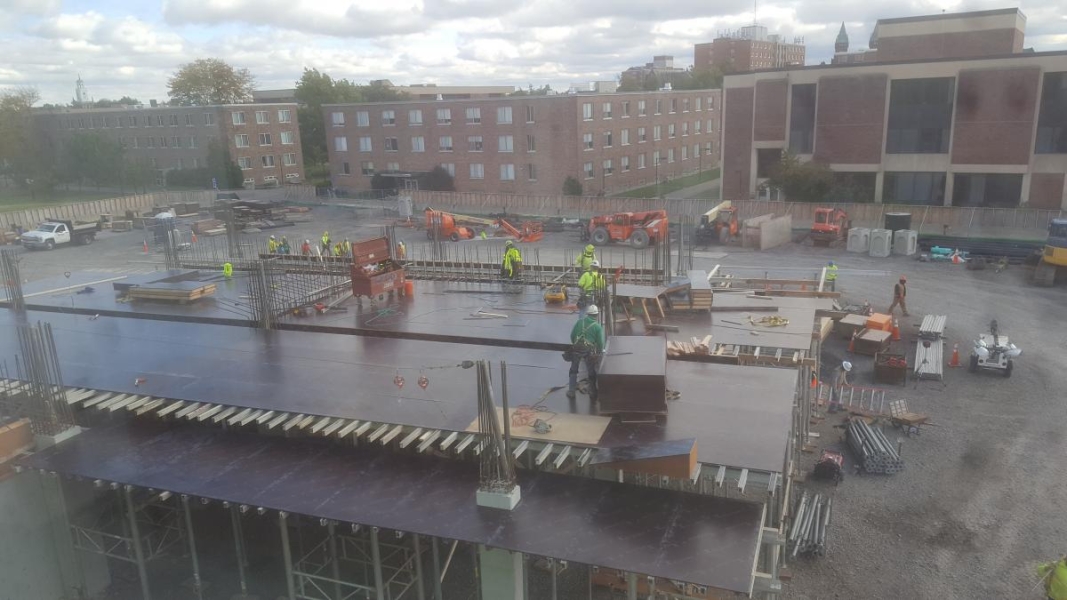 Construction workers stand on steel plates placed across the first floor of a building under construction.