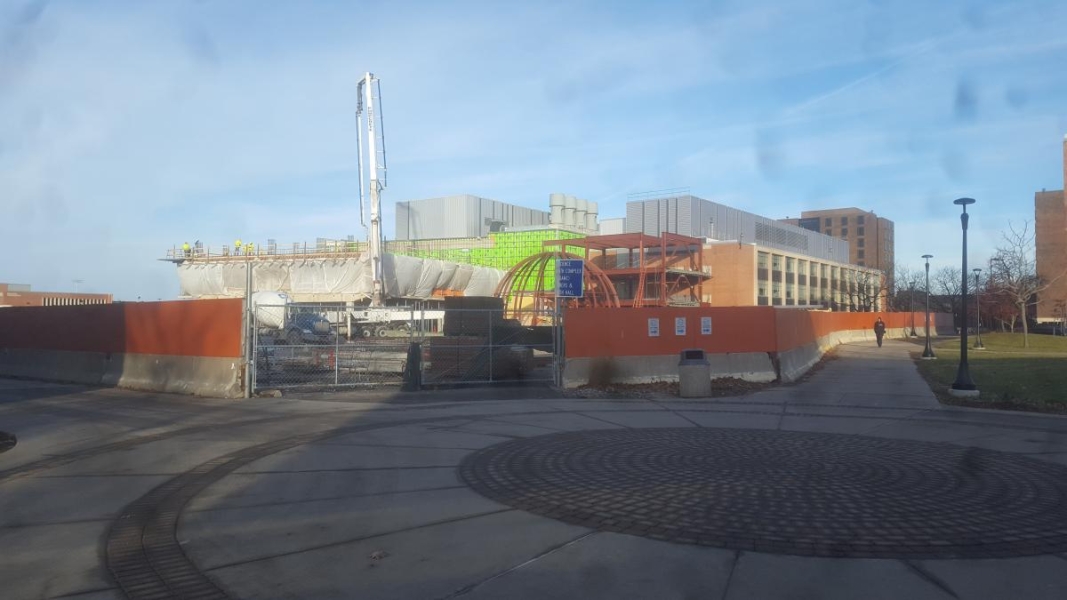 A construction site with a partially constructed building made of concrete and steel beams. A concrete truck has a long tall crane arm. Tarps are over part of the building.