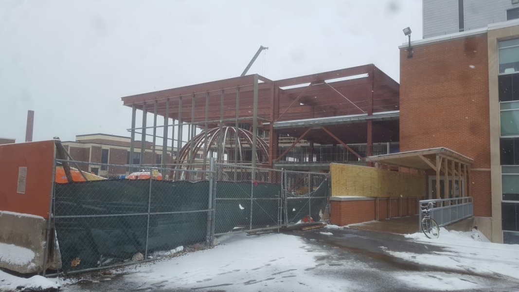 A building under construction with a large steel frame surrounding a dome made of steel beams. There is snow on the ground.