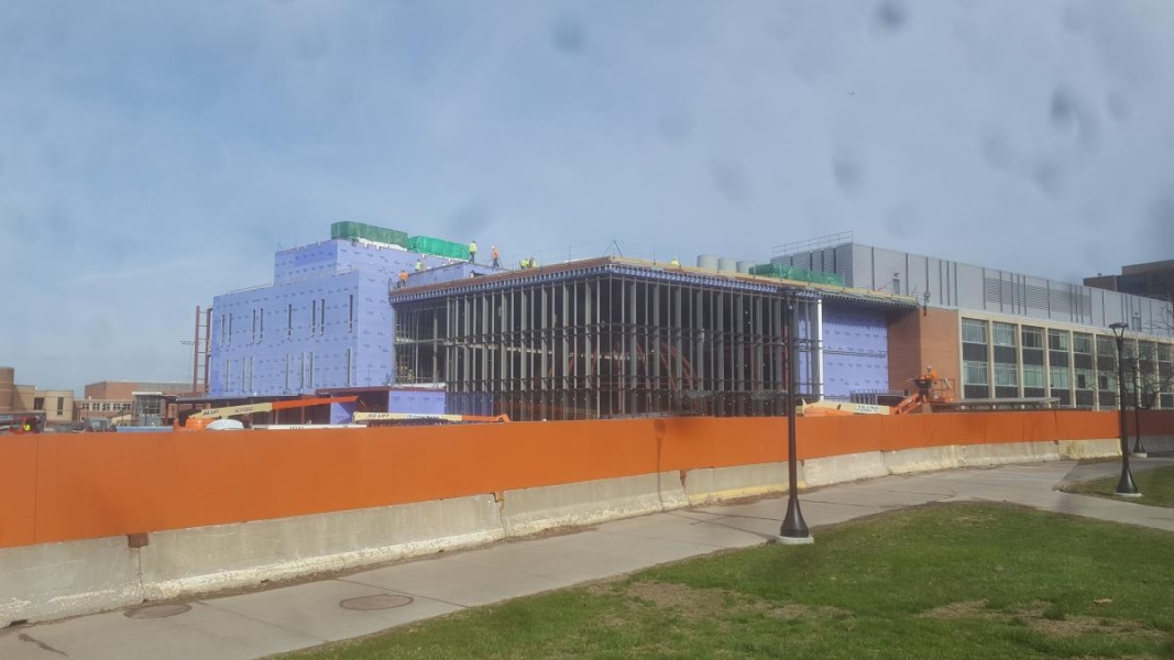 A partially constructed building that has walls enclosing part of it, a steel frame surrounding a steel globe, and some windows on both parts of the building.