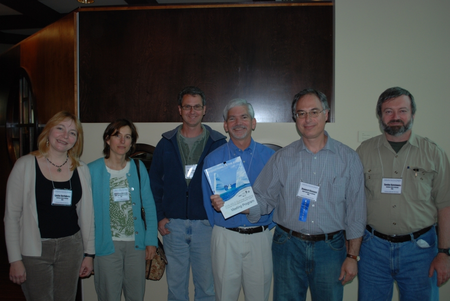 six people pose for a picture indoors, while one holds up a program booklet