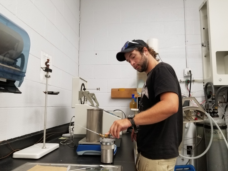 A person stands in a lab in front of a bomb calorimeter