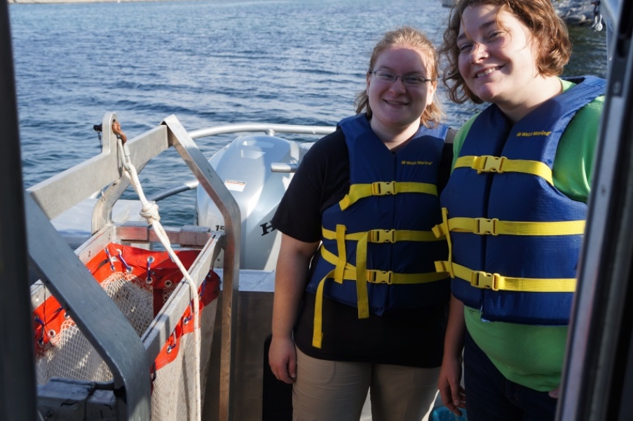 Two people stand on the back of a boat next to a rectangular net with a narrow opening.