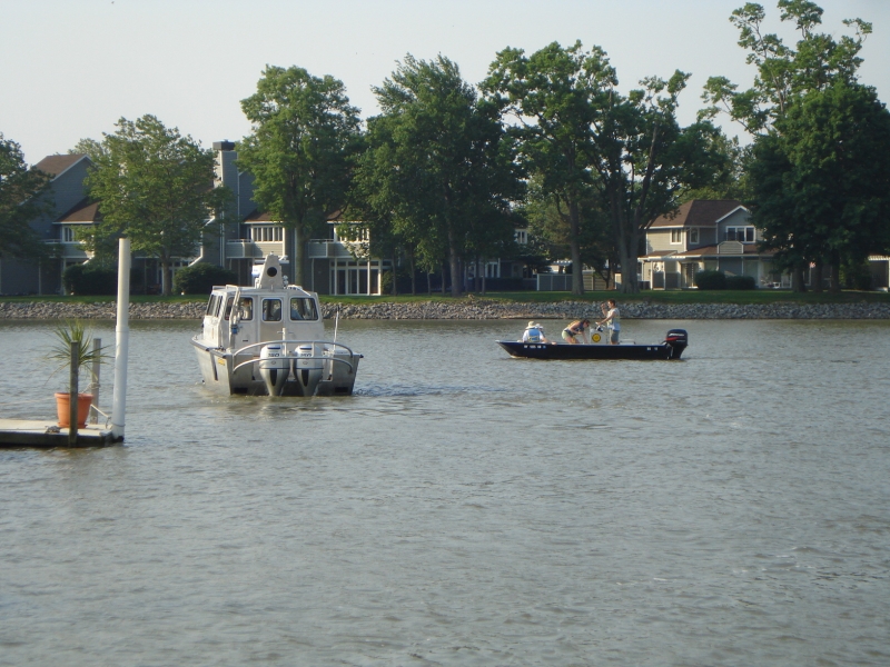 A boat with a cabin and a small workboat with three people, in the water near a dock