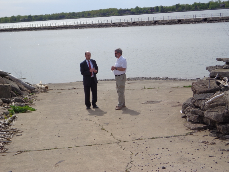 Two people stand on a boat launch by the water.