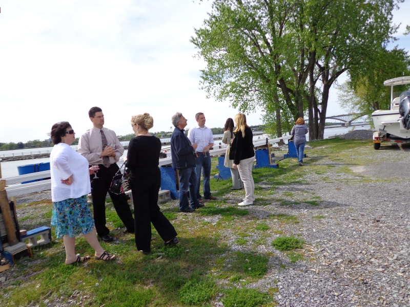 People standing outside by the waterfront. There is an experiment trough set up behind them, and a boat on a trailer nearby.