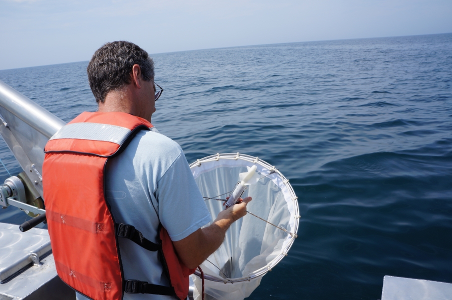 A person in a life jacket on a boat holds up a round net and looks at a device in the mouth of the net