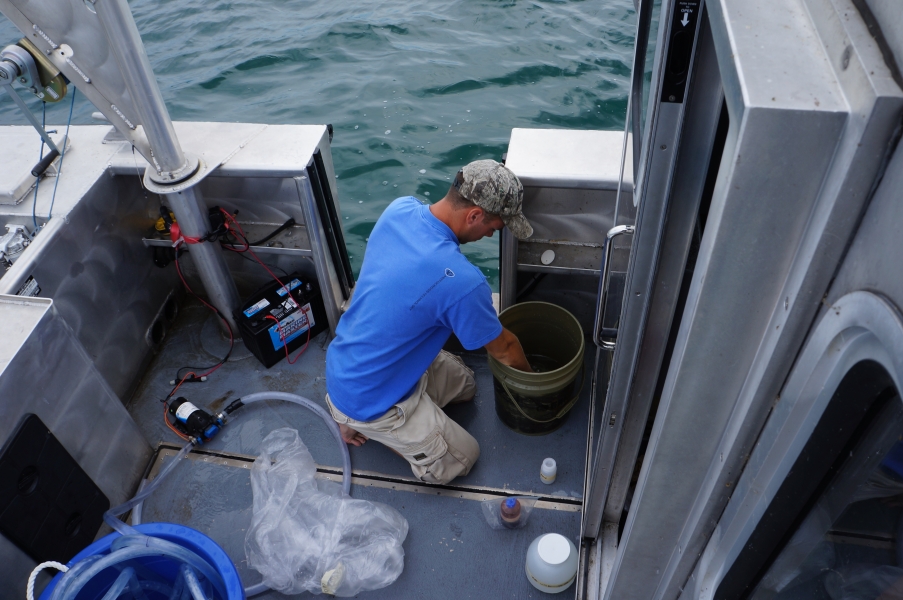 A person on a boat reaches into a bucket. There are several small bottles on the deck around them