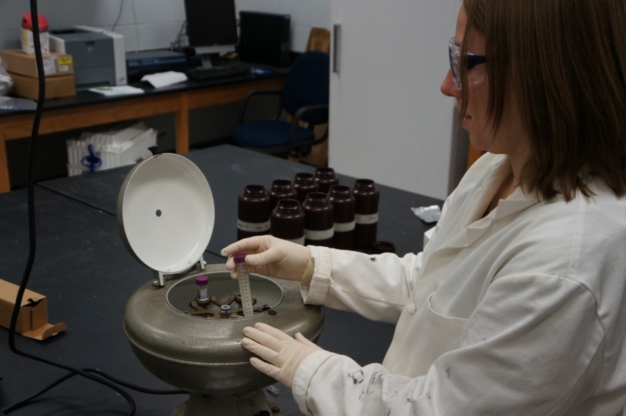 A person in a lab coat puts a sample tube in a centrifuge