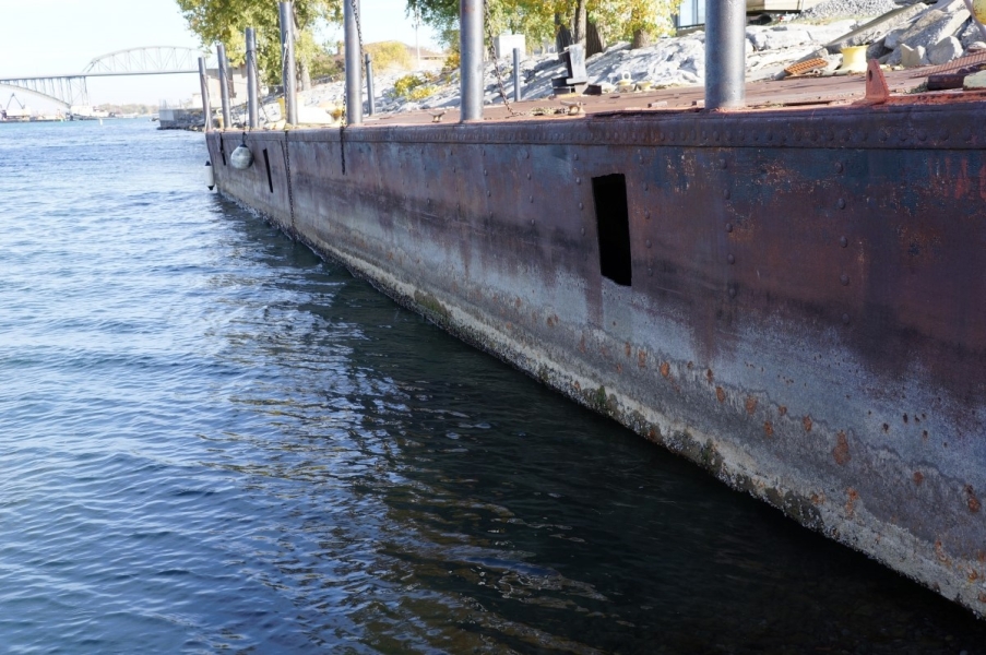 A barge that is used as a dock. The high water level is visible at least a foot above the water, and the water is below the bottom of the barge by a few inches.