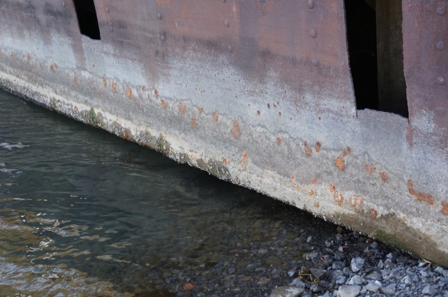 The bottom of a barge that is used as a dock. The high water level is visible at least a foot above the water, and the water is below the bottom of the barge by a few inches.