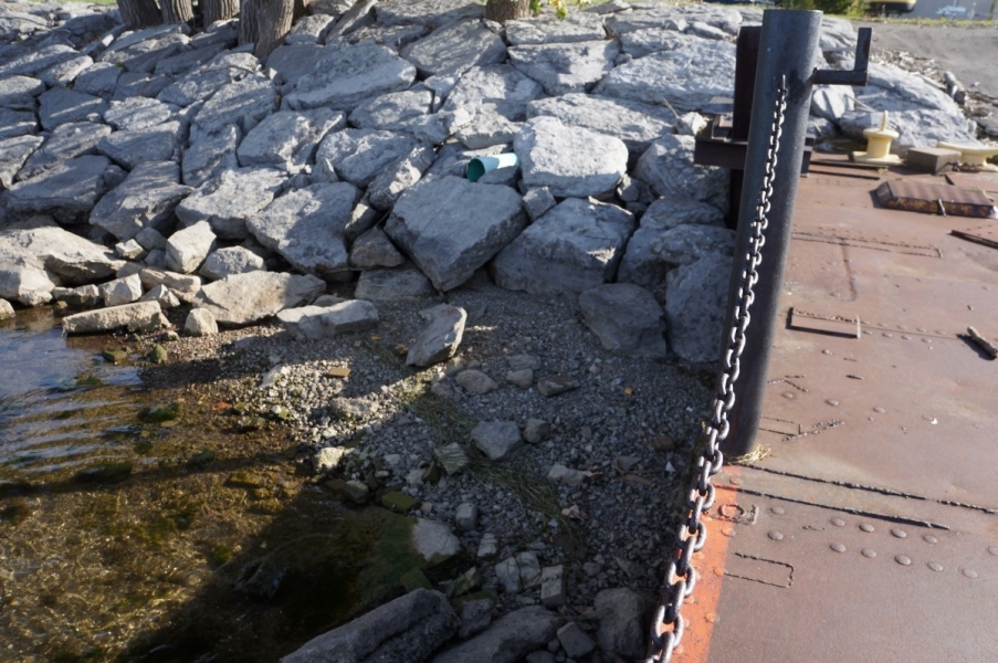 The area next to a dock has a neatly arranged stone shoreline, and gravel with some shallow water.