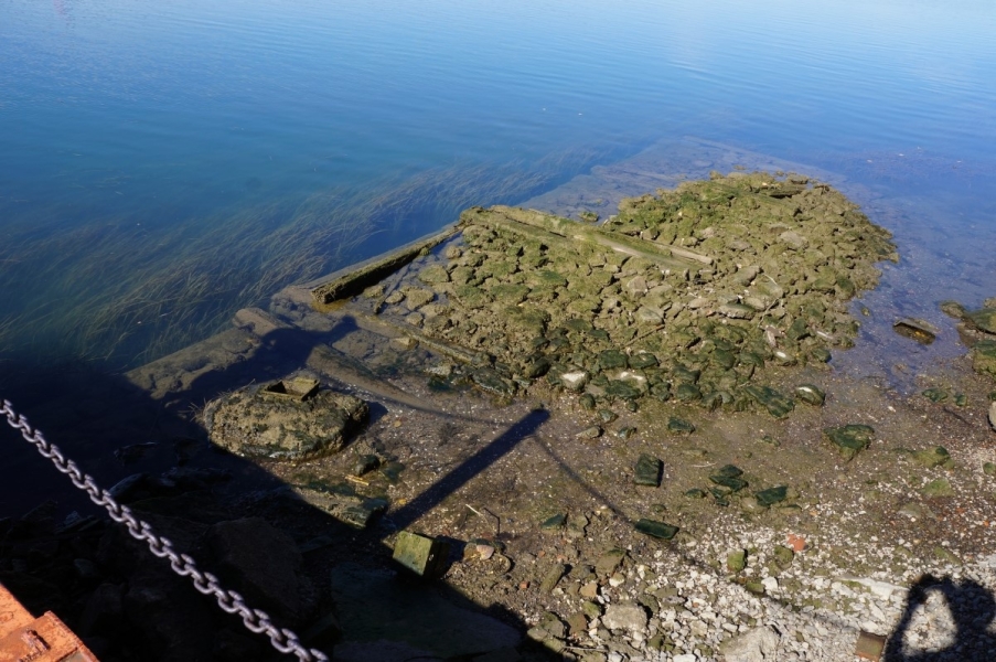 almost the entire shape of algae-covered stone and wood cribbing is visible above the water.