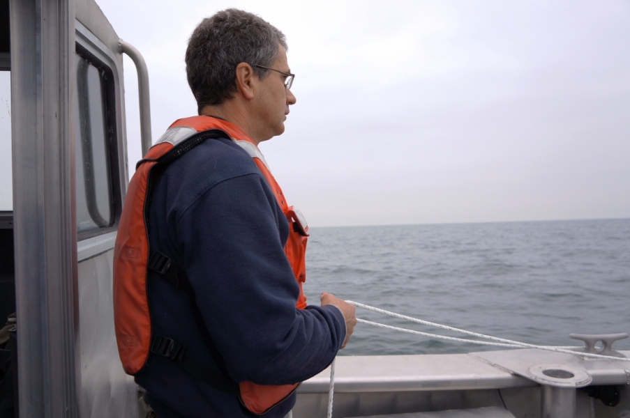 A person in a life jacket stands on the back of a boat holding a rope