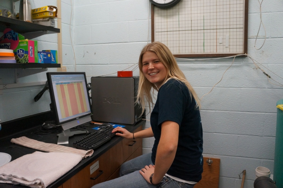 A smiling person sits at a computer in a lab.