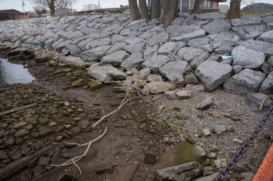 The entire shape of algae-covered stone and wood cribbing is visible above the water, as well as several feet of shoreline below the normal water level.