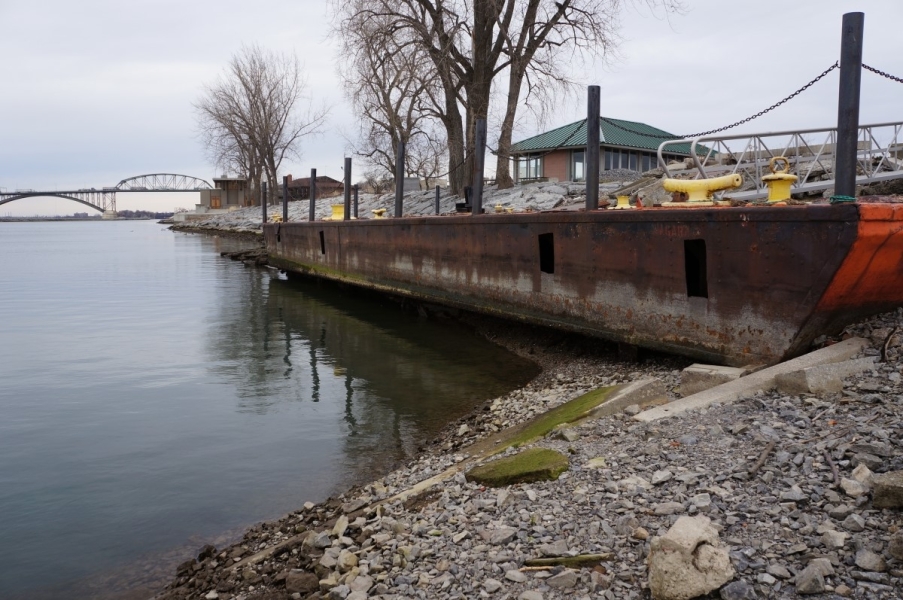 A barge that is used as a dock. The high water level is visible at least a foot above the bottom, and the water is below the bottom of the barge by at least a foot.