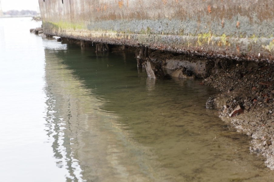 A barge that is used as a dock. The water is below the bottom of the barge by about a foot and the sediment below the barge is slightly eroded and visible