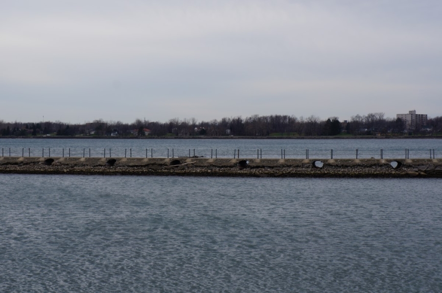 A breakwall that separates the canal from the the river. Several feet of gravel are visible below the culverts in the breakwall. There is an area of wet gravel above the current water level, as if the water level has fallen.