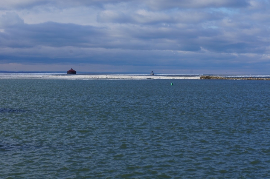 Ice coats the break wall, but the water nearby is clear of ice. There is a roundhouse in the water on the other side of the ice.