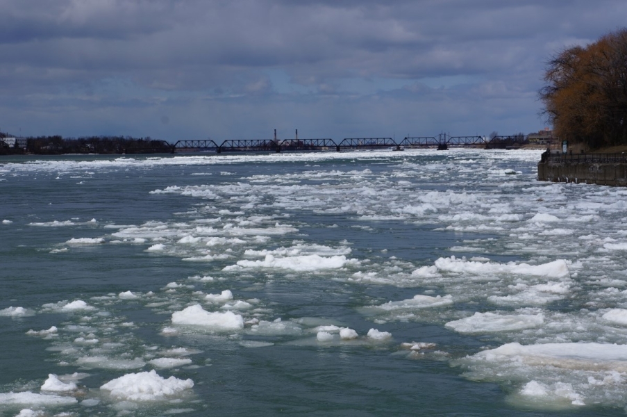 Large chunks of ice in the river. There is a train bridge in the distance.