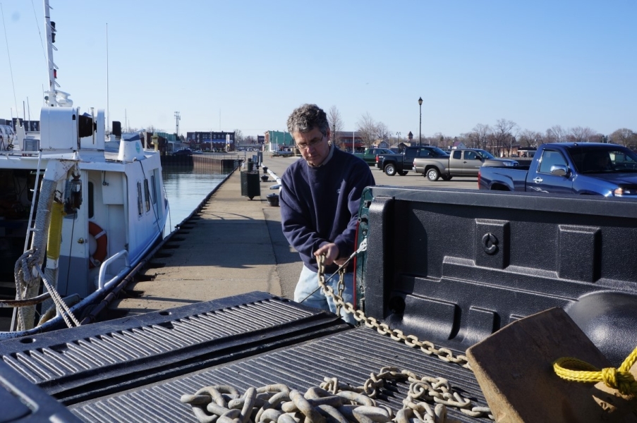 A person pulls a chain off the back of a pickup truck. There is a boat nearby.