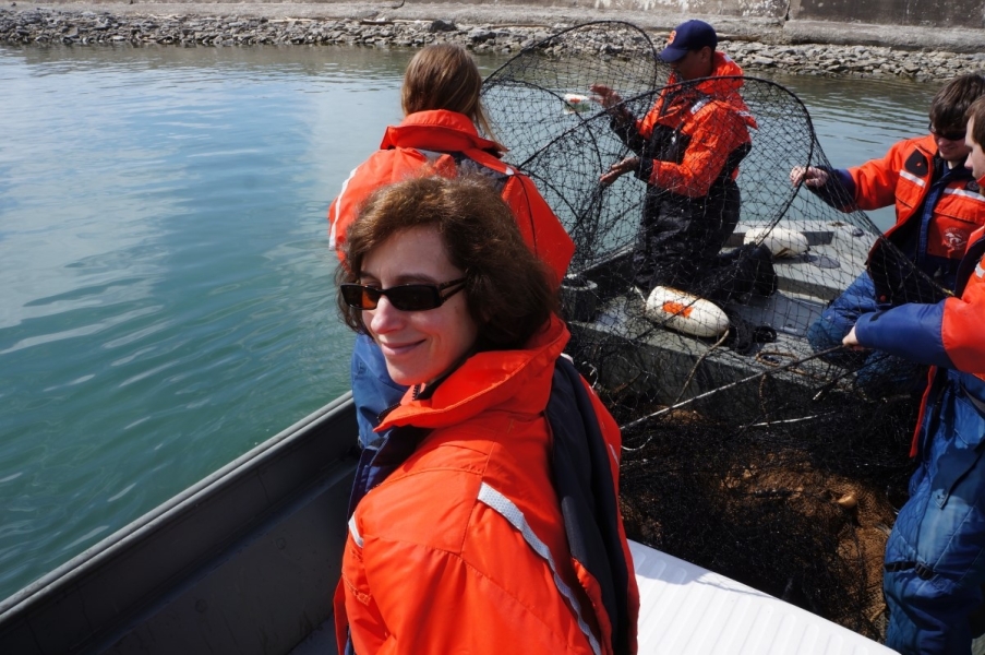 A person in the foreground smiles while four people pull a hoop net aboard a boat.