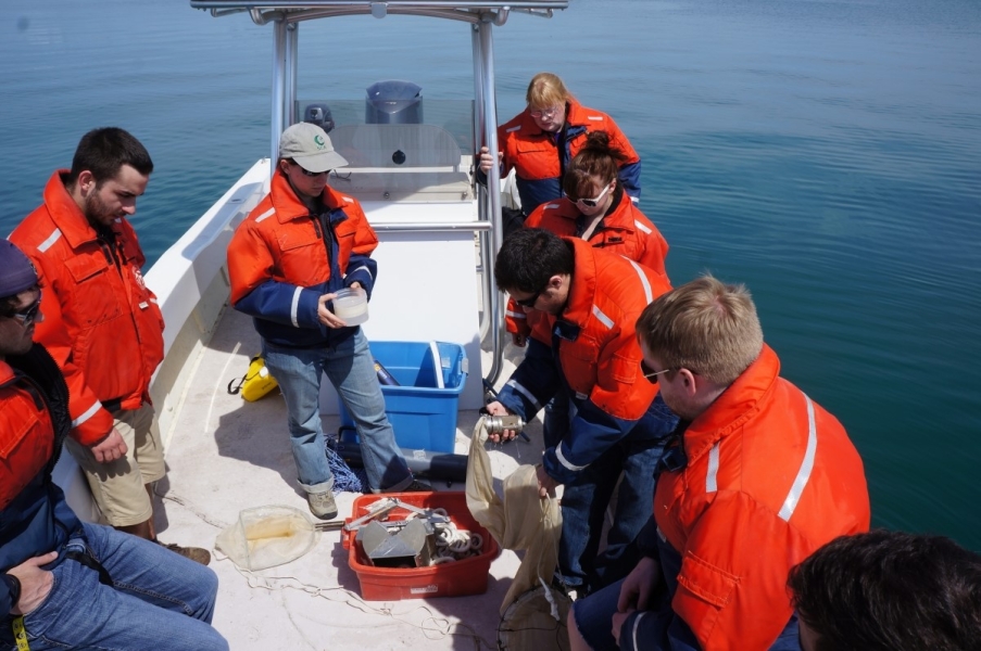 People on a boat looking at equipment. One holds a net