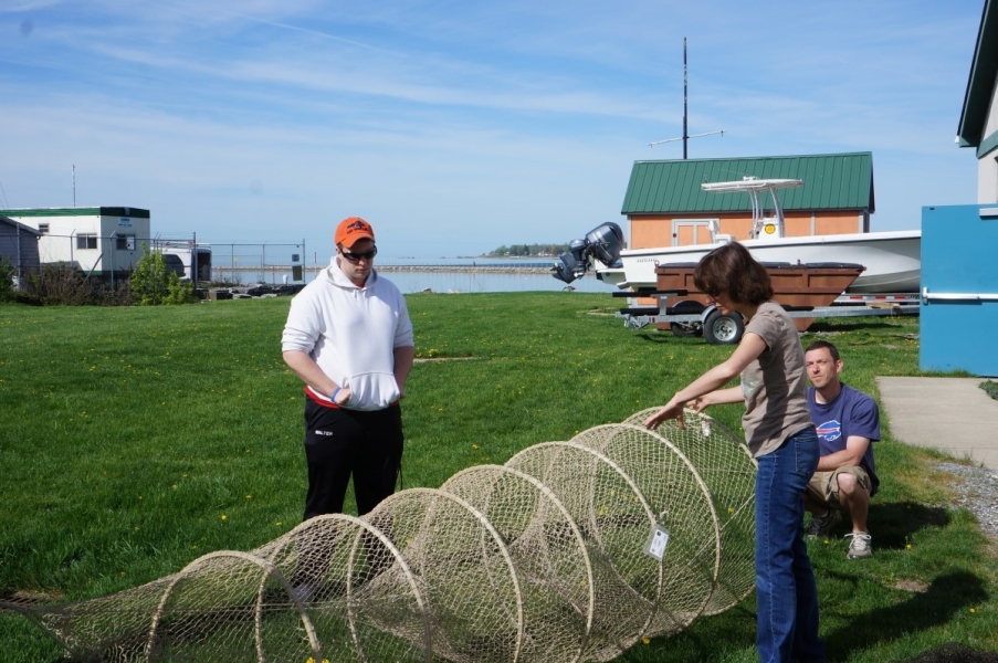 Three people stand around a net with many hoops spaced along its length set up in a field.