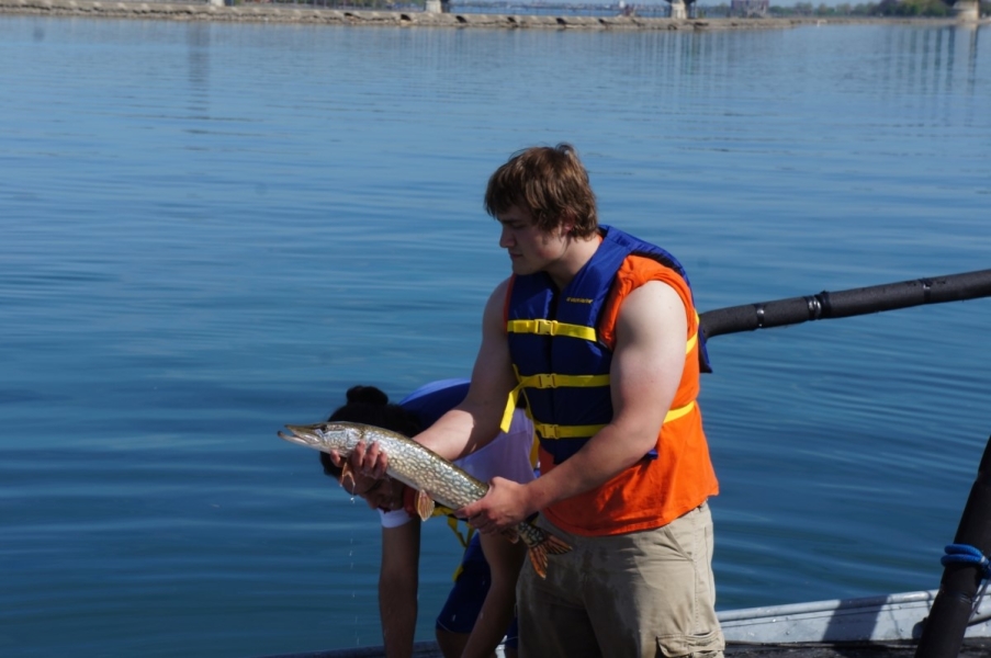 A person in a life jacket stands in front of water holding up a large speckled fish