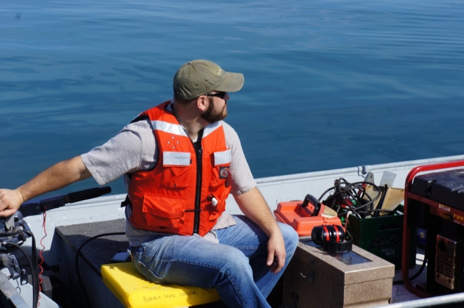 A person sitting the the back of a boat, operating the motor.