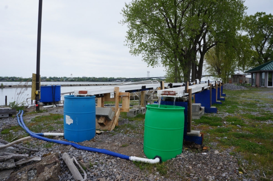 two long thin troughs held up about three feet from the ground with a round barrel at the end of each, set up on the waterfront.