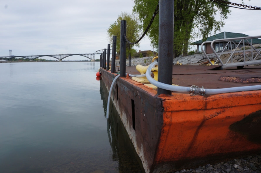 A hose is draped over a metal dock and into the water.