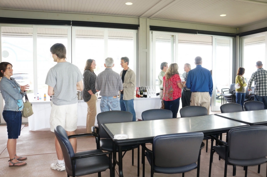 People mingling by the refreshments set up by the glass walls of a pavilion.