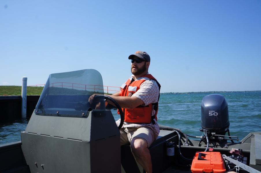 A person sits at the controls of a boat at a boat launch