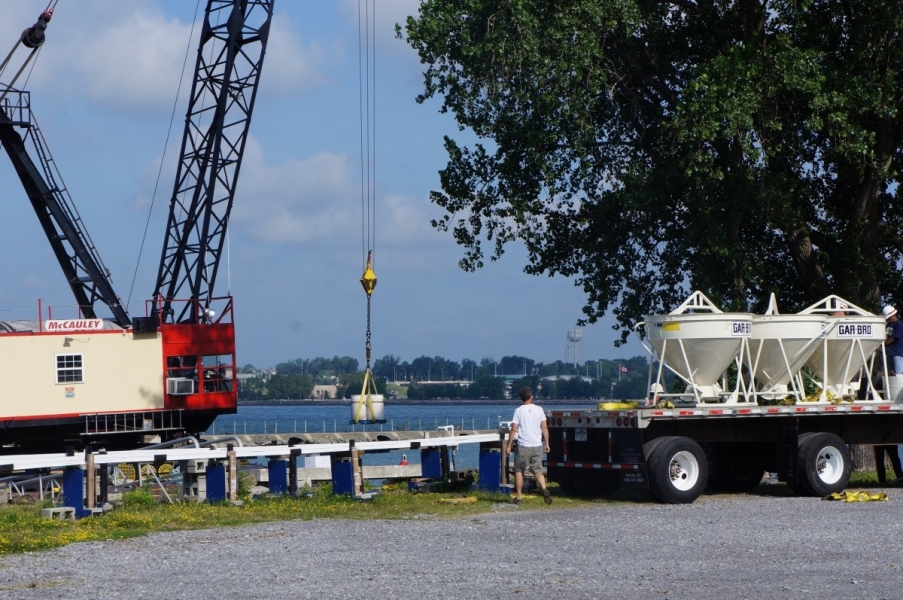 A crane on a barge lifts some equipment. The flatbed of a truck with some other equipment is visible.