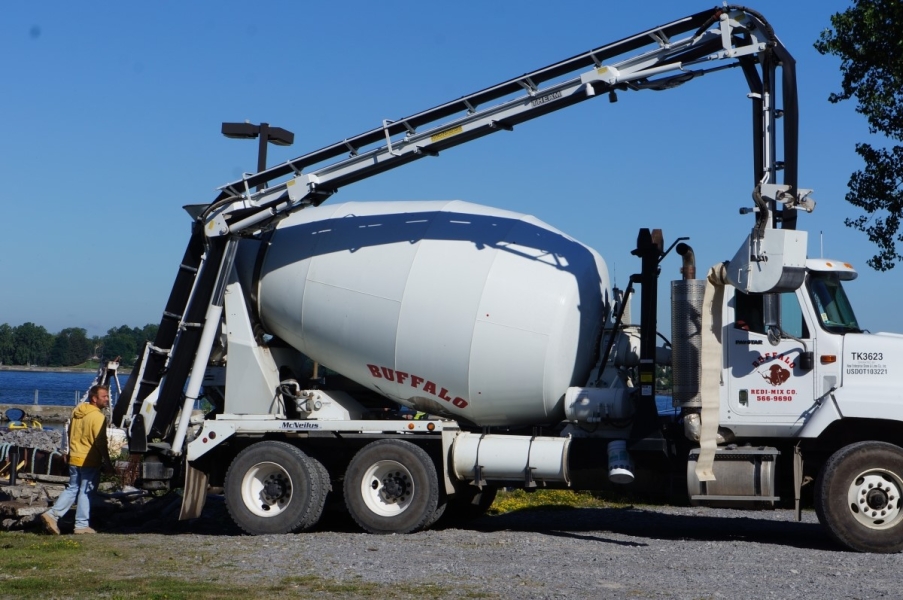 A cement truck with a long arm to deliver concrete arrives near the waterfront.