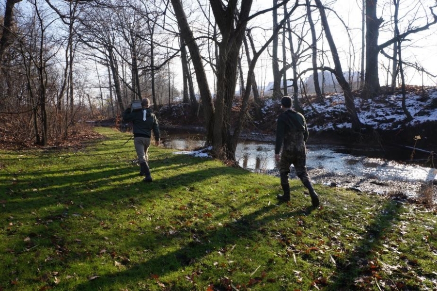 Two people walk in the grass near a creek in winter.